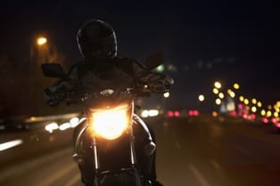 photo of motorcycle at night with headlight on and rider wearing a helmet